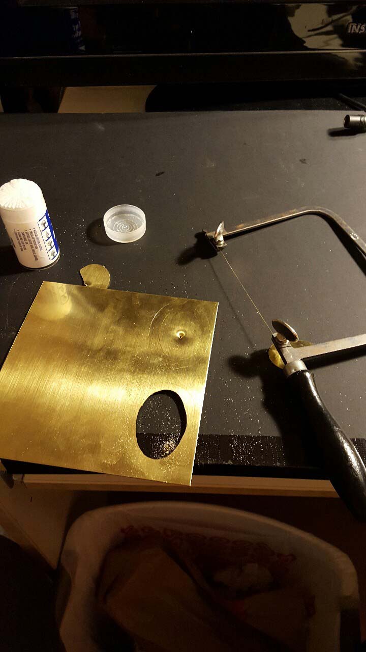 Hand-sawing ovals out of a sheet of brass for the shoe buckles.