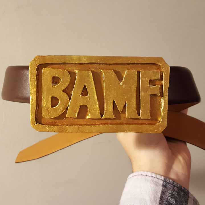 Handmade gold belt buckle that says "BAMF", attached to a brown belt.