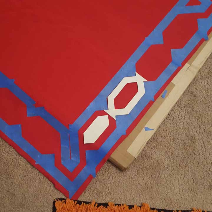 Red fabric for the serape, with painters tape marking out the pattern for painting over.