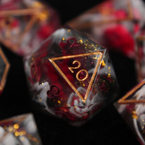 A set of dice with opaque white and black swirls, gold glitter flakes, and bright red flowers.