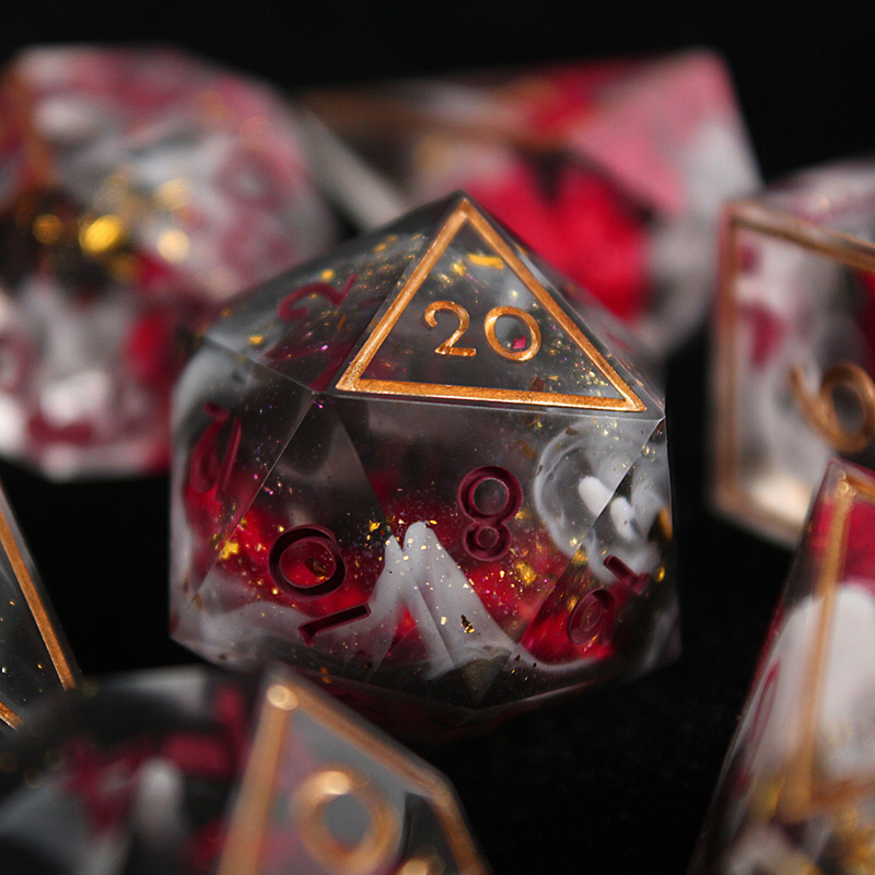 A set of clear dice with opaque white and black resin swirls. They include gold glitter and bright red flowers, and are inked in burgundy and gold.