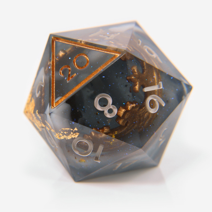 A dark translucent blue-grey D20, with a gold crown embedded inside. The die is inked in off-white and gold.