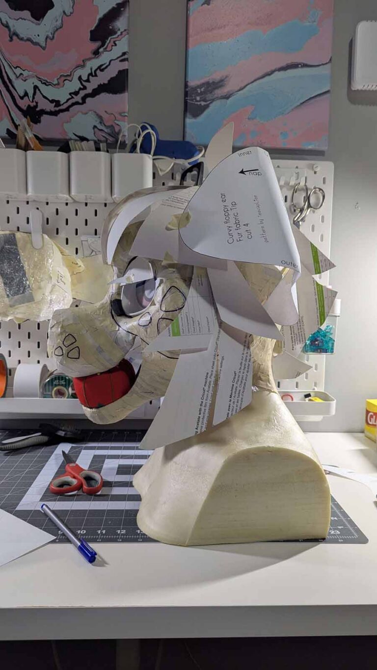 The masking tape pattern applied to the fursuit head base, with markings sketched out in marker. The ears and hair have been roughly cut out of paper and taped on to mock up the scale and placement.