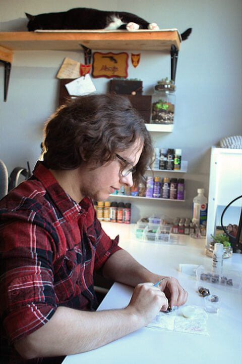 An artist painting a set of dice with a small paintbrush.