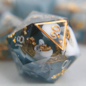 A blue-grey D20 die with gold foil and glitter, and a golden crown. It's inked in light grey and gold.